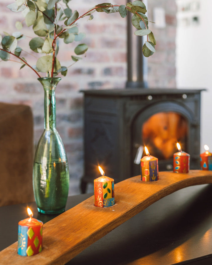 Lifestyle photo of 5 African Mineral votives in a holder made from the arch of a wine barrel!  Burning brightly with a fire place in the background.  Beautiful!  