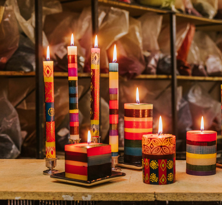 Lifestyle photo of Memphis Stripe tapers, cube, and pillar mixed with Desert Rose tapers and pillar.  All burning brightly with bags of color in the candle factory behind them.