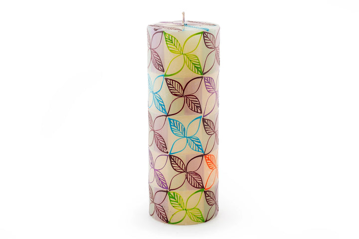 Magic Garden 3" x 8" pillar candle. The pillar is a white base with green, orange, turquoise, and lavender stripes. Overlay of pigment colors with a variety floral and leaf designs.