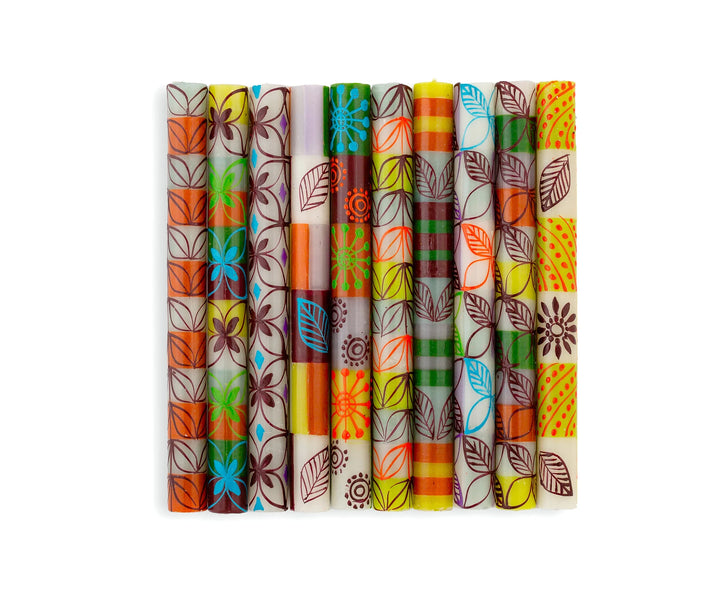 Magic Garden taper candles, photo shows all 10 designs of the collection in white base with green, orange, turquoise, and lavender stripes. Overlay of pigment colors with a variety floral and leaf designs.