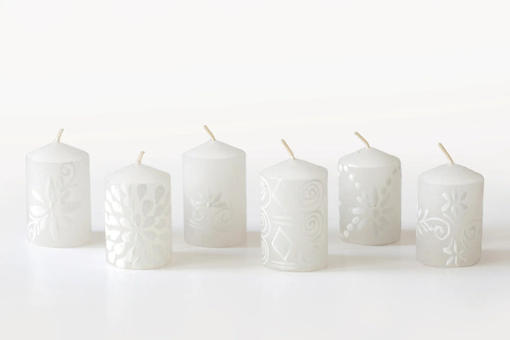 6/2" White on white votive candles. The designs include floral or graphic patterns painted in white on a white candle. Packaged in a 6-pack gift box.