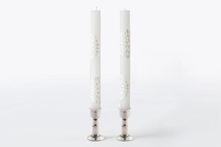 Matched pair of 9" dinner taper candles in pewter taper holders. The designs include floral or graphic patterns painted in white on a white candle. Beautiful as they burn as the candle lights from within and shows the artistry on the candle.